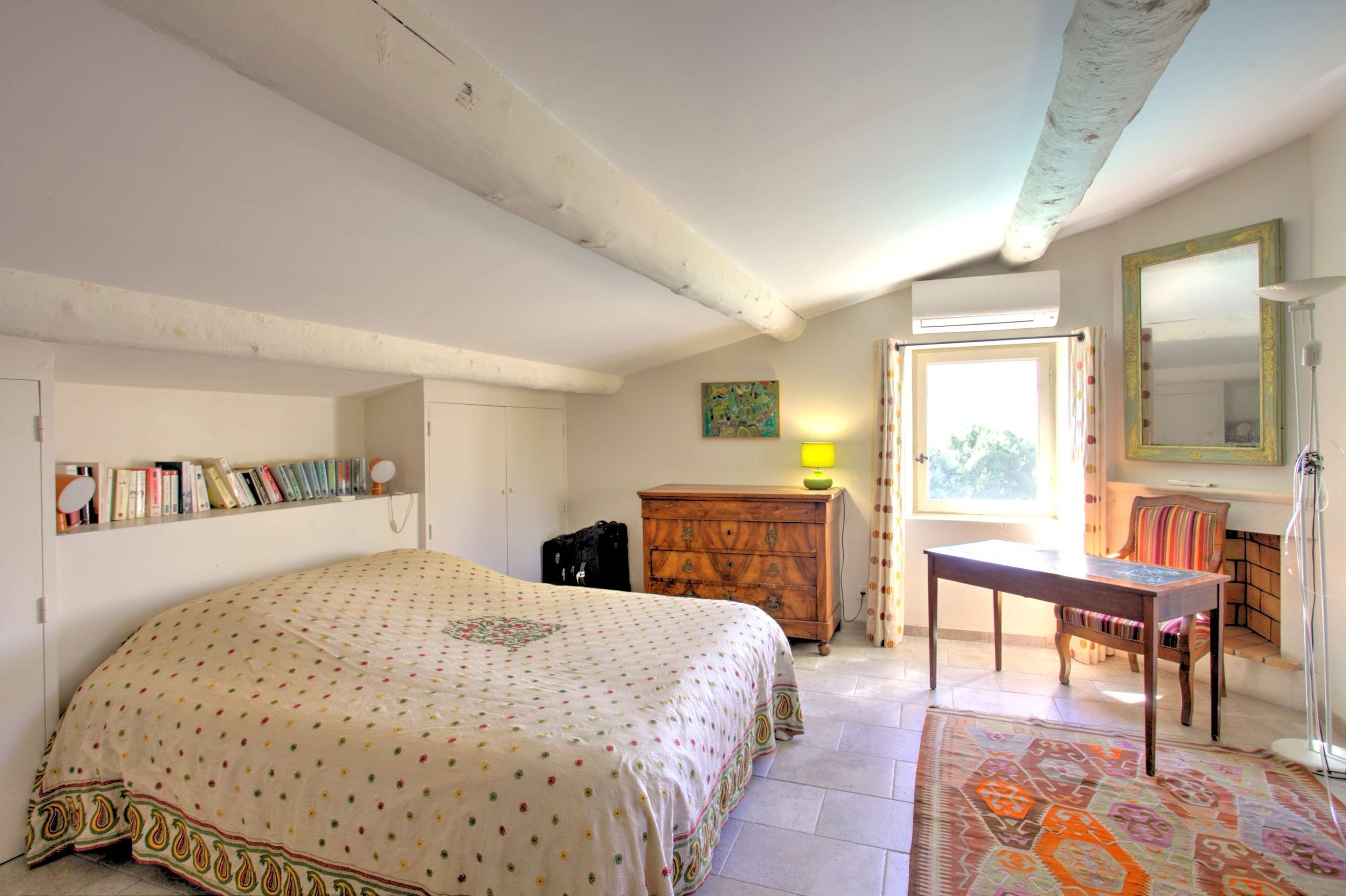 A bedroom with a bed, a wooden dresser, a desk, a chair, a mirror, and a bookshelf.