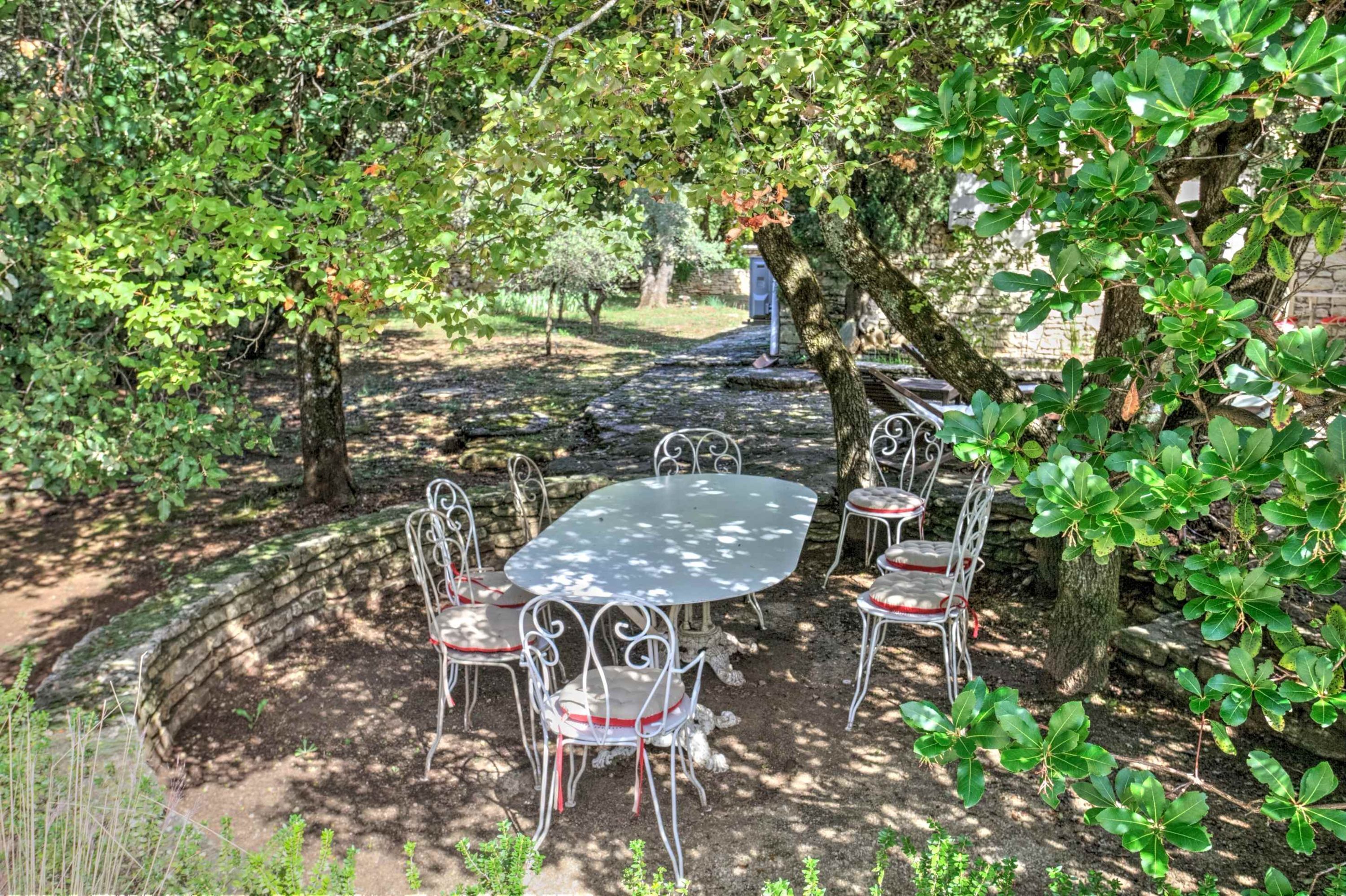 An outdoor garden with a stone pathway, metal tables and chairs, and lush greenery.