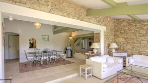 A spacious living area with a stone wall, a dining table with chairs, a white sofa, and a small side table with a lamp. - La Garrigue de Gordes (Gordes)