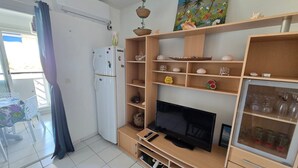 Una sala de estar con televisor, estanterías con adornos, refrigerador y un comedor con mesa y sillas.
