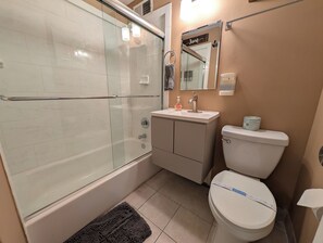 A bathroom with a glass-enclosed shower, a sink with a soap dispenser, a toilet with a lid, and a towel rack. - Urban Oasis Luxe King Suites  City Views (Atlanta)