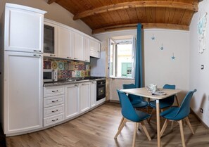 A kitchen with white cabinets, a colorful backsplash, and a dining area with blue chairs. - Daenerys Loft Old Town Alghero (Alghero)