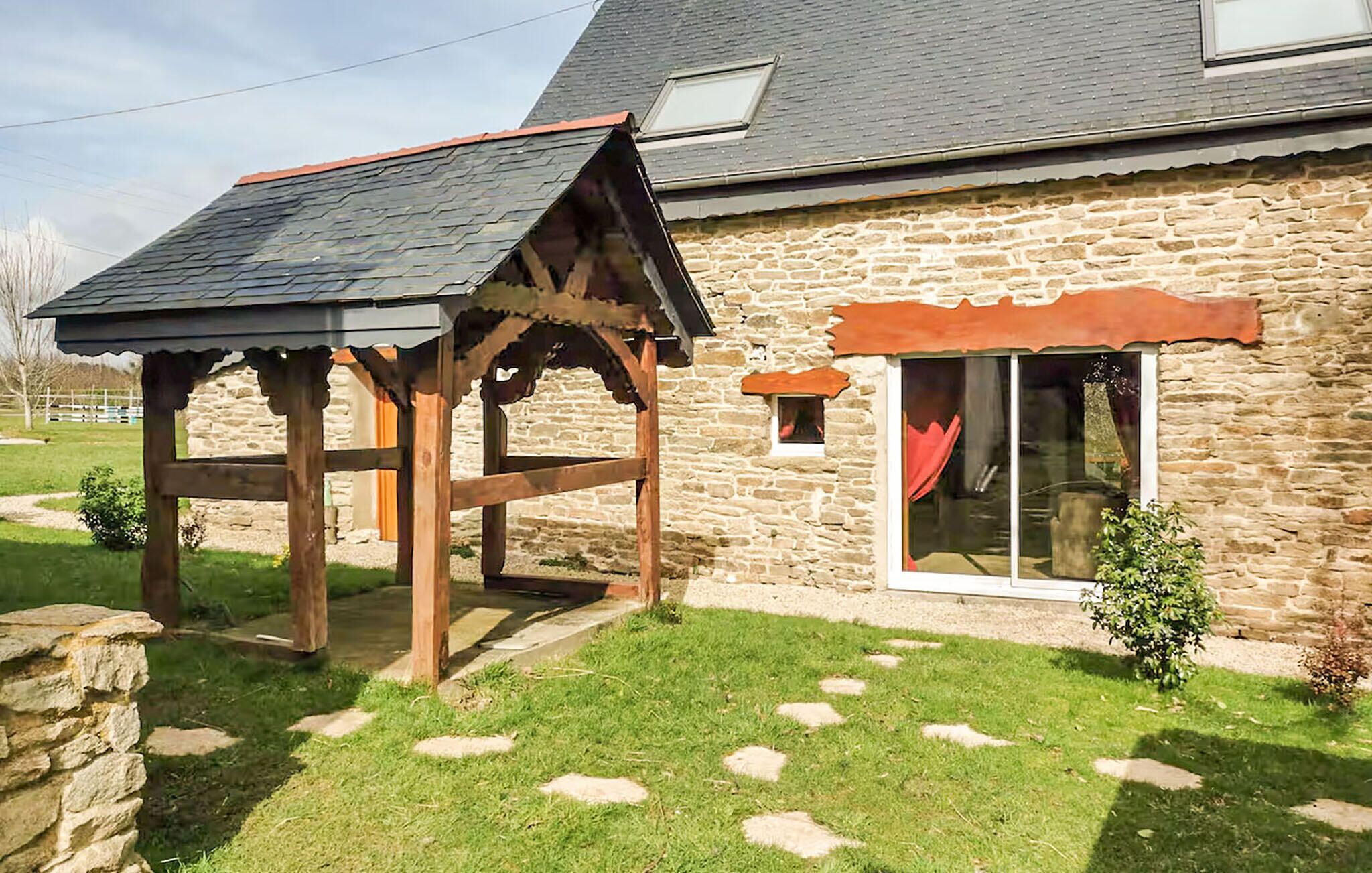A stone house with a wooden pergola and a window with a red curtain.
