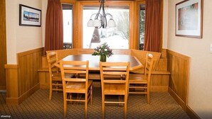 Uma sala de jantar com mesa e cadeiras de madeira, um lustre e uma janela com cortinas.