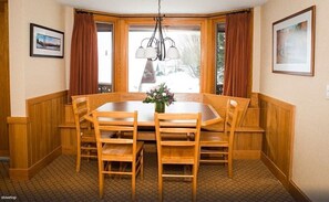 Ein Essbereich mit Holztisch und Stühlen, einer Deckenleuchte und einem Fenster mit Vorhängen.