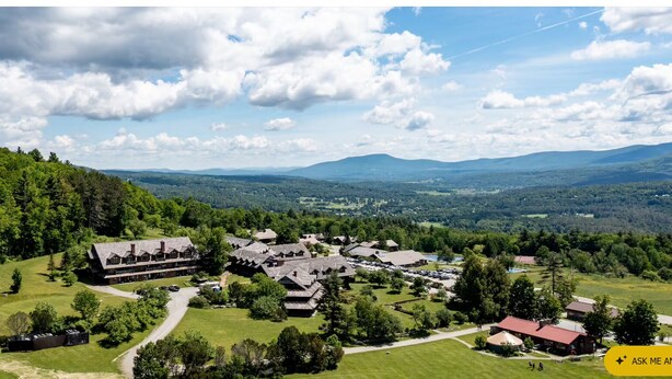 Vista aérea de um resort com vários edifícios, área de estacionamento e vegetação ao redor.