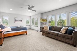 A bedroom with a bed, a sofa, a ceiling fan, and large windows. - Family Riverhouse with Hot Tub (Columbia Falls)