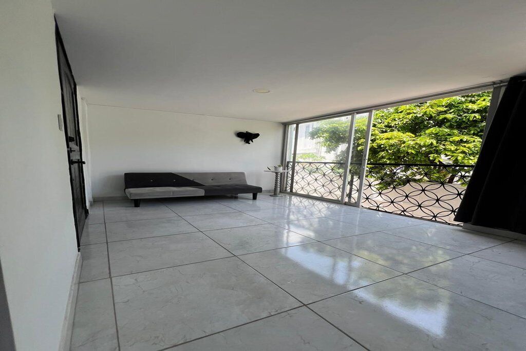 Varanda ampla com sofá cinza, grade de metal e vista para o verde.