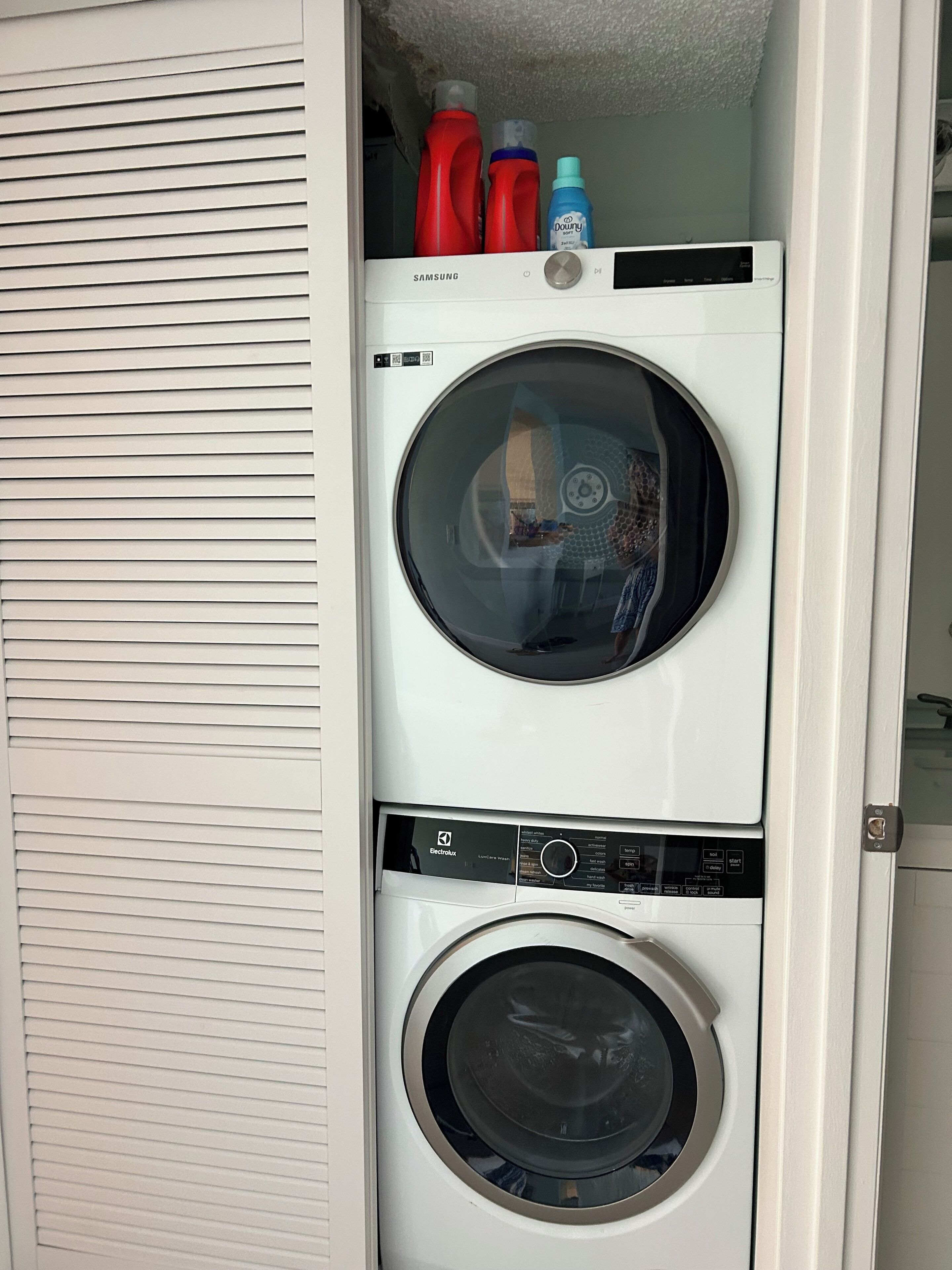 Un appareil combiné lave-linge et sèche-linge, avec les panneaux de commande et les bouteilles de lessive placés sur le dessus.