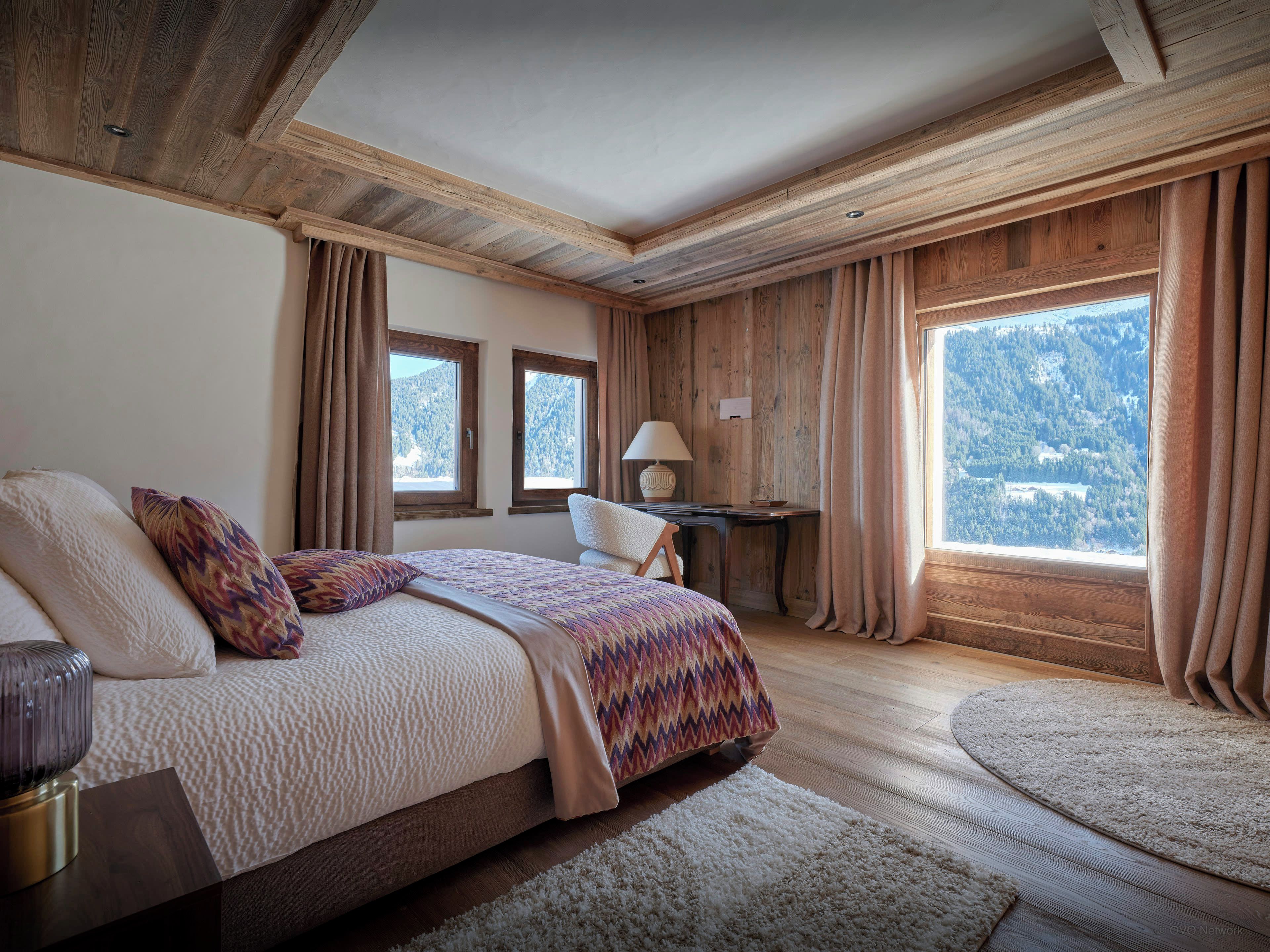 Ein Schlafzimmer mit Bett, Schreibtisch, Stuhl und großen Fenstern mit Blick auf die Berge.