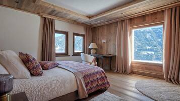 Une chambre à coucher comprenant un lit, un bureau, une chaise et de grandes fenêtres donnant sur une vue imprenable sur les montagnes.