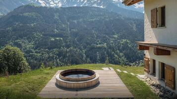 A wooden deck with a hot tub, a mountain view, and a building with wooden shutters.