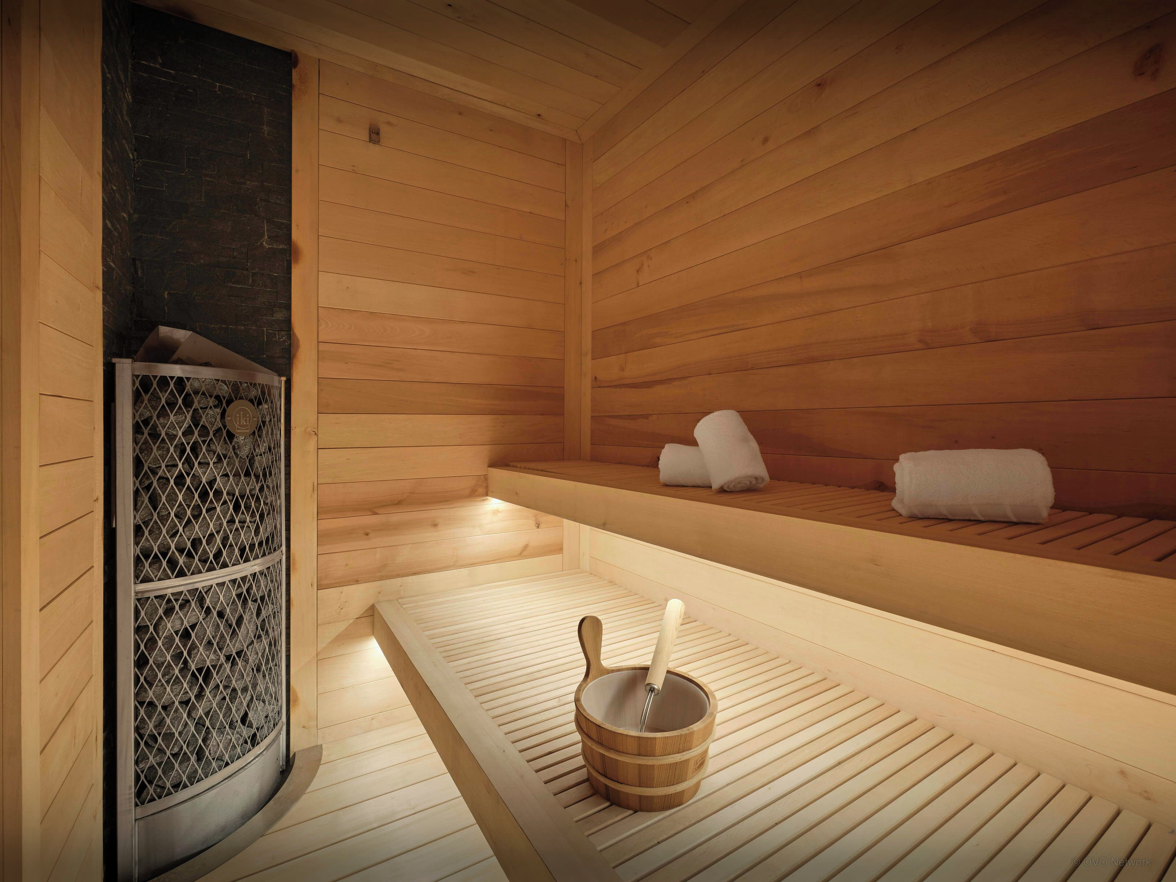 A sauna with wooden benches, a stone wall, and a wooden bucket with a mallet.