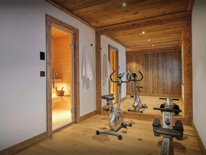 A gym with two stationary bikes, a treadmill, and a sauna visible through an open door.