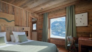 Ein Zimmer in einer Holzhütte mit einem Bett, einem Schreibtisch und einem Fenster mit Blick auf die Berge.
