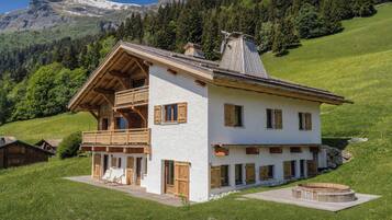 A white chalet with wooden balconies, a wooden deck, and a stone fireplace.