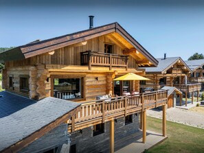 Una cabaña de troncos con balcón, mobiliario exterior y una chimenea de piedra.
