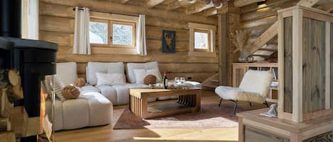 A log cabin interior with a fireplace, a sofa, a coffee table, and a chair.