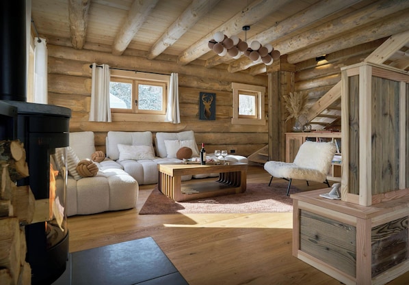L’intérieur d’une cabane en rondins, avec une cheminée, un canapé, une table basse et un fauteuil.