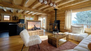 Et interieur i en hytte med træloft, pejs, fjernsyn, sofa og spiseplads.