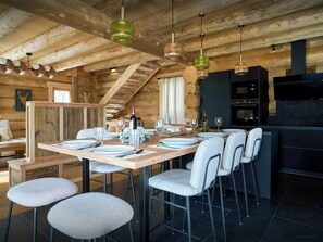 A wooden cabin interior with a dining table set for four, bar stools, a kitchen area, and a ceiling with exposed beams. - Chalet Escapade - Family-friendly chalet, near the slopes - OVO Network (Font-Romeu-Odeillo-Via)