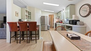 Cozinha moderna com área de jantar, apresentando uma mesa de madeira, cadeiras e um relógio grande na parede.