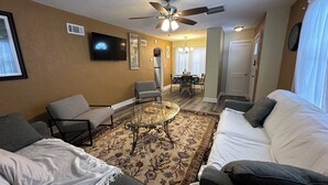 Un salon comprenant un canapé, des fauteuils, une table basse et un téléviseur fixé au mur.