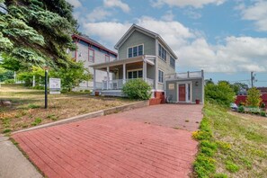 Ein zweistöckiges Haus mit Veranda, einer kleinen angeschlossenen Garage und einem Ziegelweg, der zum Eingang führt.