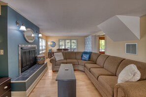 A living room with a fireplace, a sectional sofa, a coffee table, and a dining area with a table and chairs. - Hendrickson House - Downtown Bayfield, WI (Bayfield)