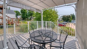 Une terrasse extérieure couverte, dotée d’une table ronde en métal et de chaises, le tout entouré d’une rambarde blanche.