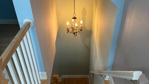 Un escalier en bois orné d’un lustre, avec des rampes blanches et un mur bleu.