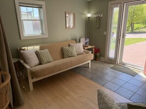 A room with a beige sofa, a small table, a floor lamp, a window, and a door leading outside. - Carriage @ Hendrickson House (Bayfield)