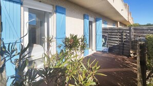 Una casa con contraventanas azules, una terraza de madera y un jardín con plantas.