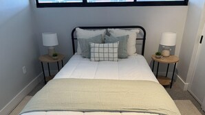 A neatly made bed with a white comforter and a quilted blanket, flanked by two bedside tables with lamps and decorative items.