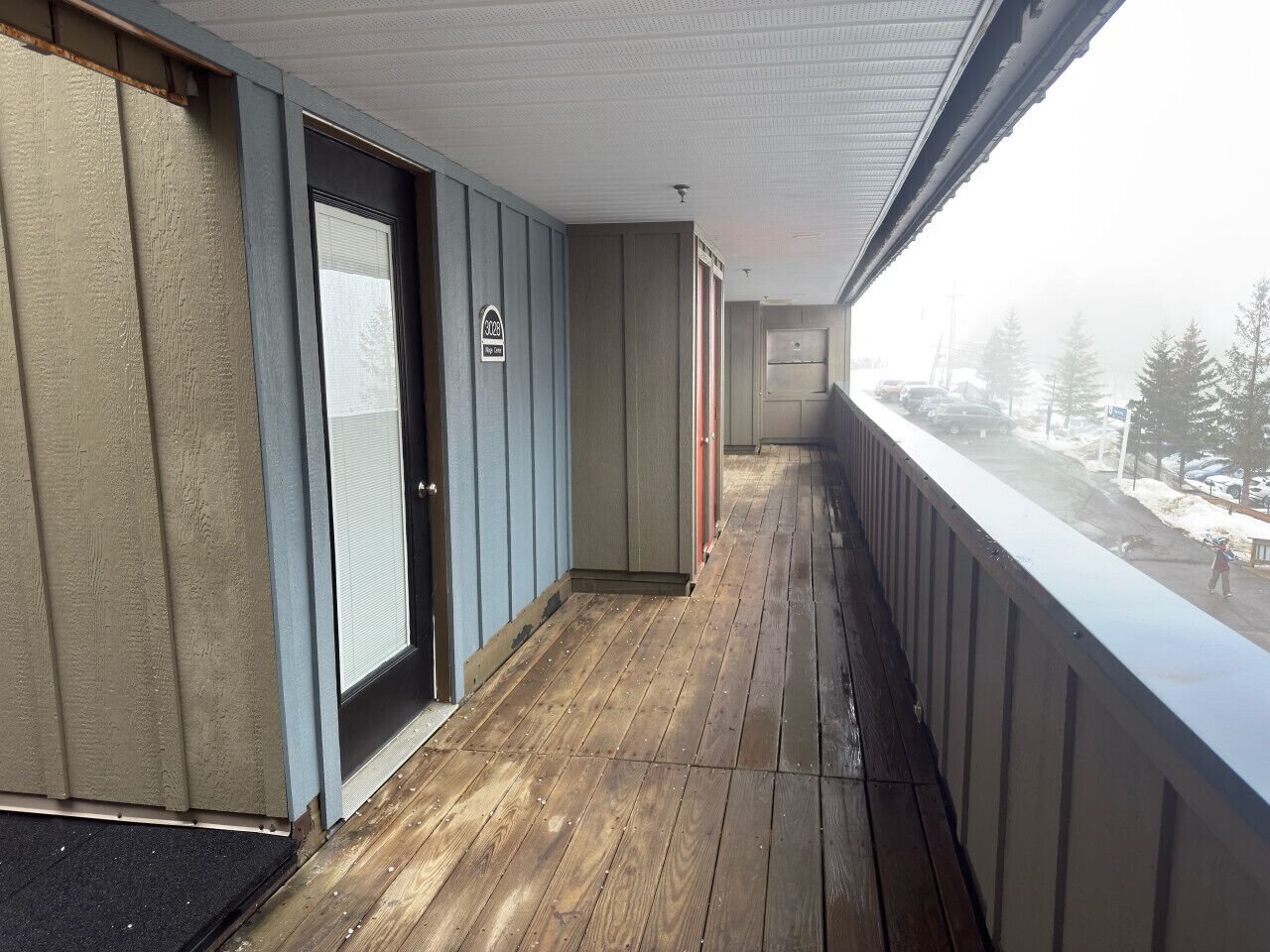 A covered outdoor area with a wooden floor, a door, and a view of a snowy landscape.