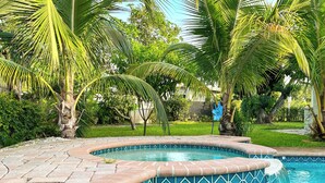 A swimming pool with a tiled edge, surrounded by palm trees and greenery. - Tranquil 4-bedroom house with heated pool and spa in Fort Lauderdale (Fort Lauderdale)