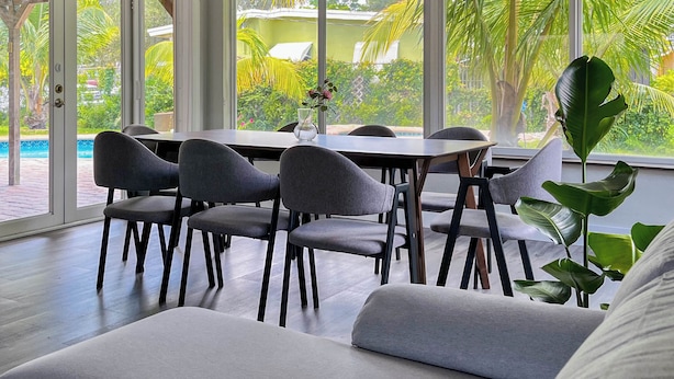 A modern dining area with a large table and chairs, large windows with a view of a swimming pool and greenery. - Tranquil 4-bedroom house with heated pool and spa in Fort Lauderdale (Fort Lauderdale)