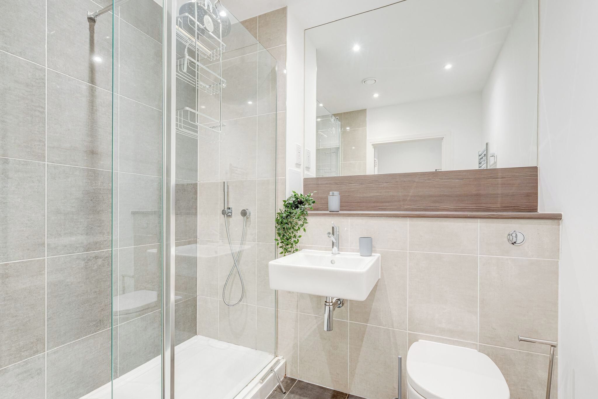A modern bathroom with a glass shower enclosure, a white sink, and a wooden vanity.