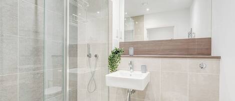 A modern bathroom with a glass shower enclosure, a white sink, and a wooden vanity.
