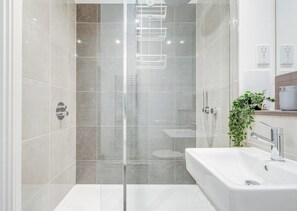 Une salle de bain moderne avec une douche à parois de verre, une baignoire blanche et un lavabo agrémenté d’une plante verte à proximité.