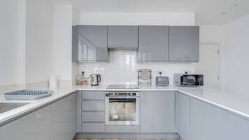 A modern kitchen with grey cabinets, a built-in oven, a microwave, and a kettle.