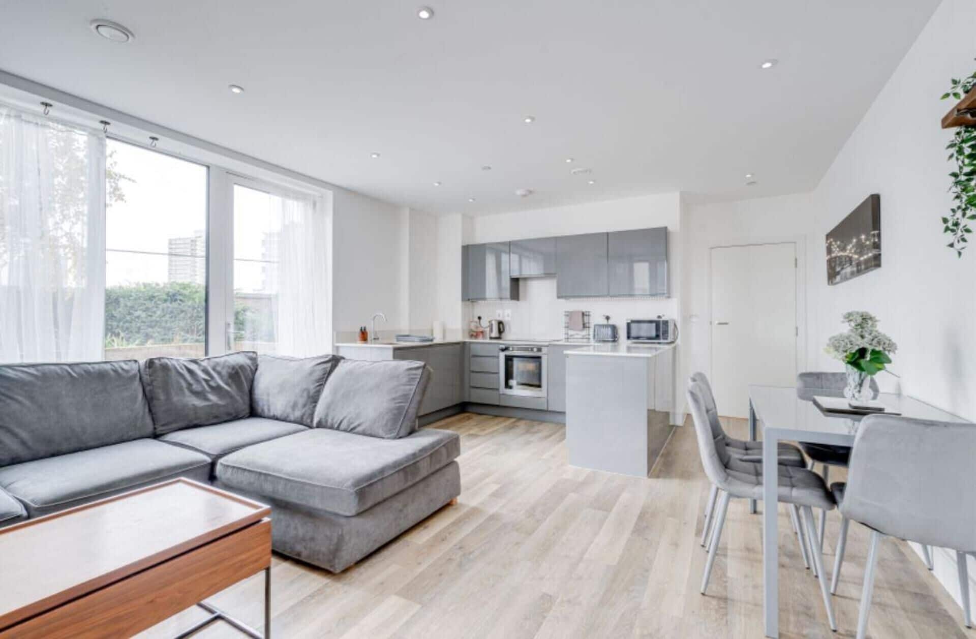 Eine moderne Wohnung mit grauem Sofa, einem Essbereich und einer Küche mit grauen Schränken.