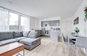 Un appartement moderne avec un canapé gris, un coin repas et une cuisine aux meubles gris.