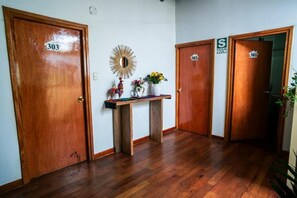 Een gang met houten vloer en drie houten deuren met de aanduidingen 303, 302 en 301. In het midden staat een klein houten tafeltje met een spiegel en decoratieve objecten.