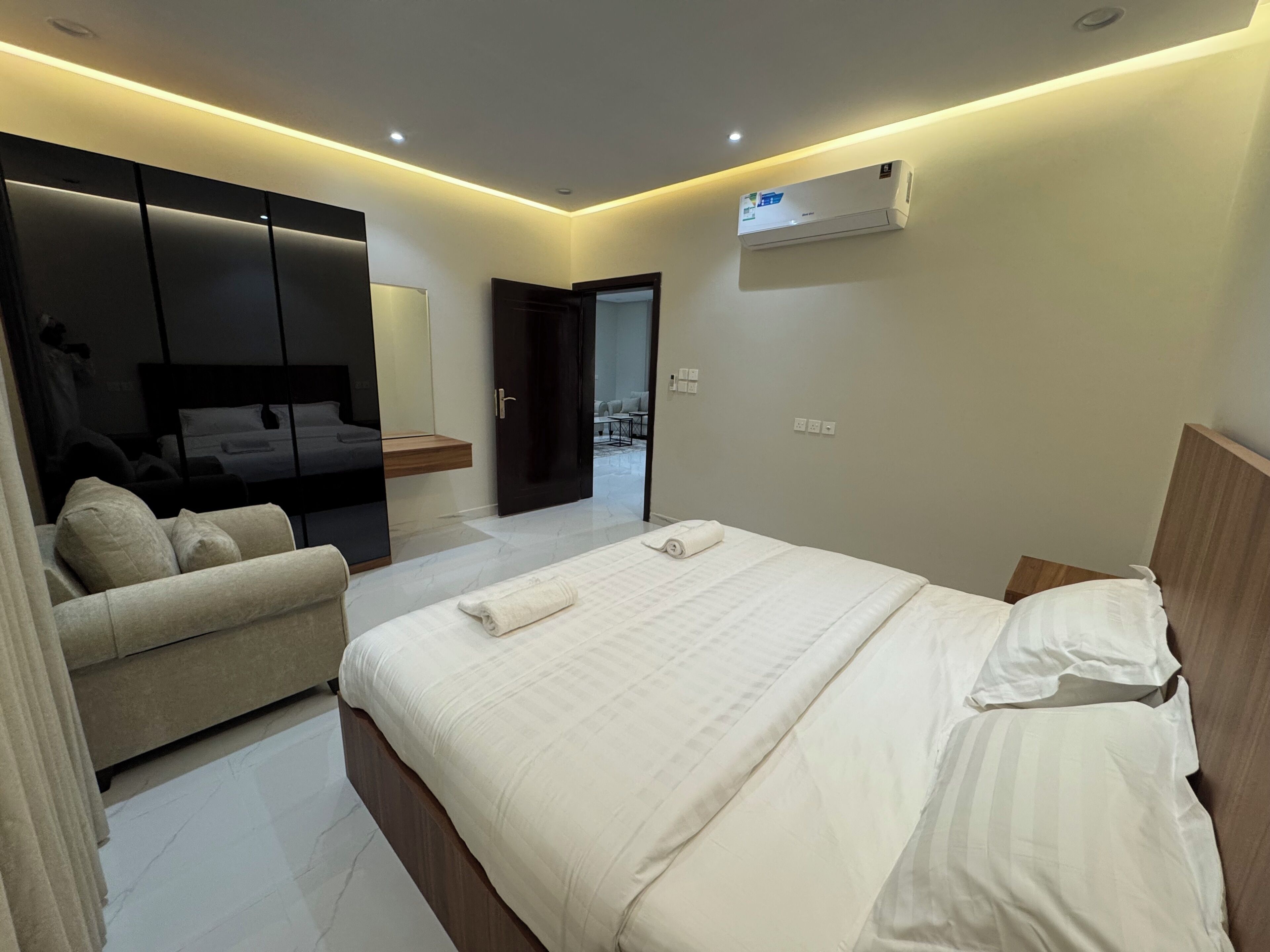 A modern hotel room with a bed, a sofa, a TV, and an air conditioning unit.