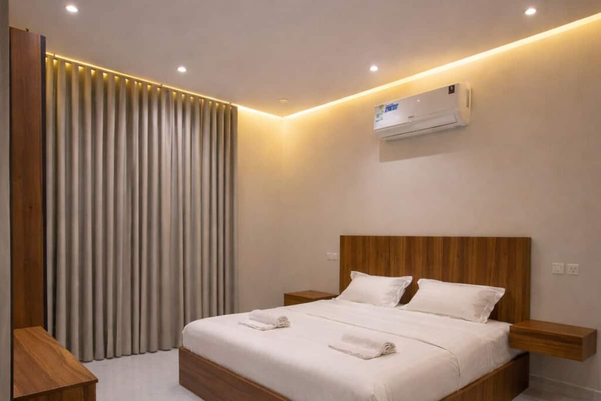 A modern hotel room with a large bed, wooden headboard, and a built-in air conditioning unit.