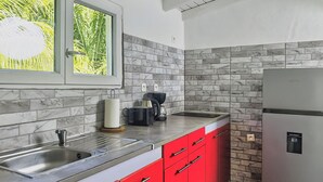A kitchen with a marble backsplash, stainless steel appliances, and red cabinets. - TERAKOTA Village Créole jacuzzis-plage (Deshaies)
