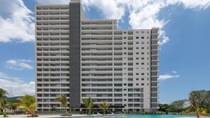 Un hôtel de grande hauteur doté de nombreux balcons, d’une piscine et d’un paysage tropical.