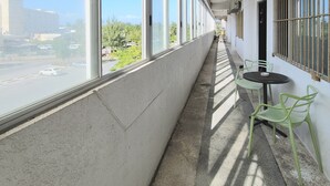 Un pasillo con grandes ventanales, una pequeña mesa con sillas y vistas a la calle y áreas verdes.