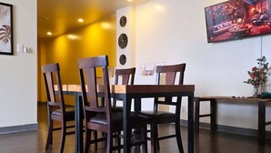 Un comedor con sillas de madera y una mesa, un cuadro en la pared y una lámpara empotrada en el techo.